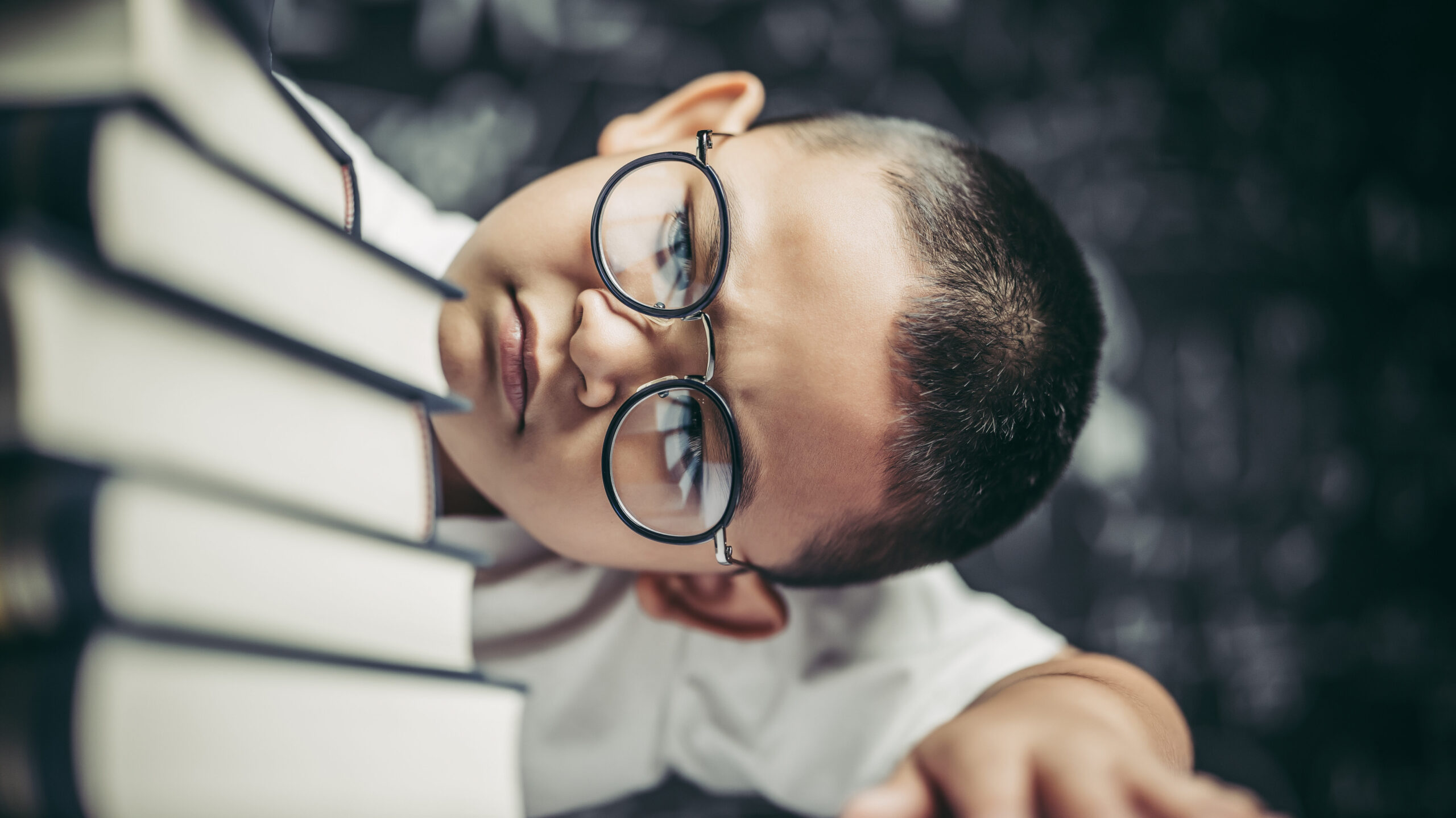 A boy with glasses sitting in the classroom counting books